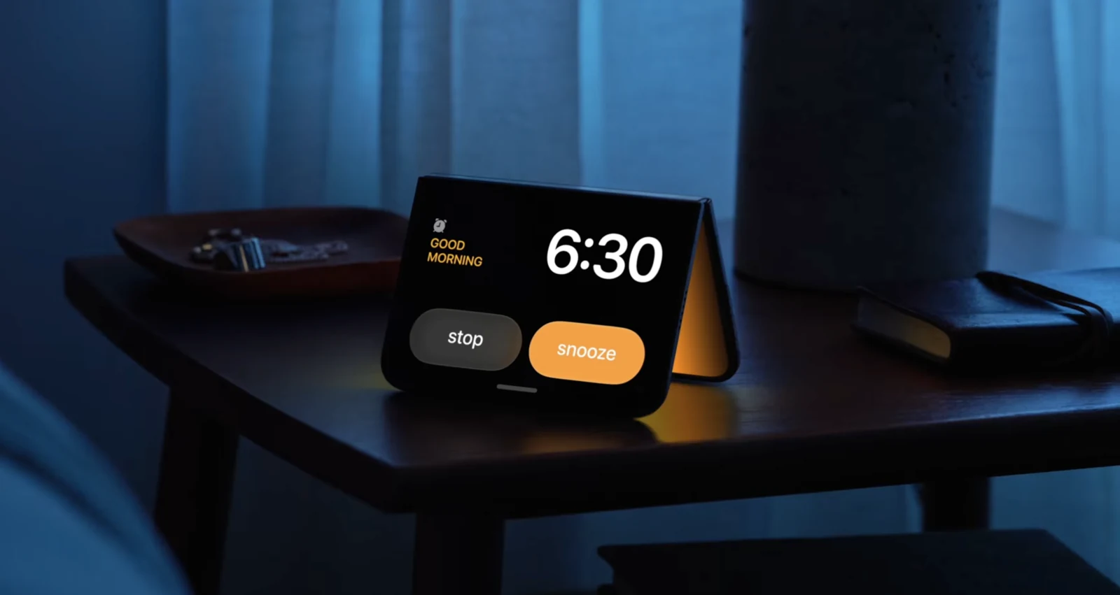 반쯤 접어 탁자 위에 세워 둔 iPhone Duo 발표 사진. 화면에 6시 30분 알람과 중지, 다시 알림 버튼이 떠 있다